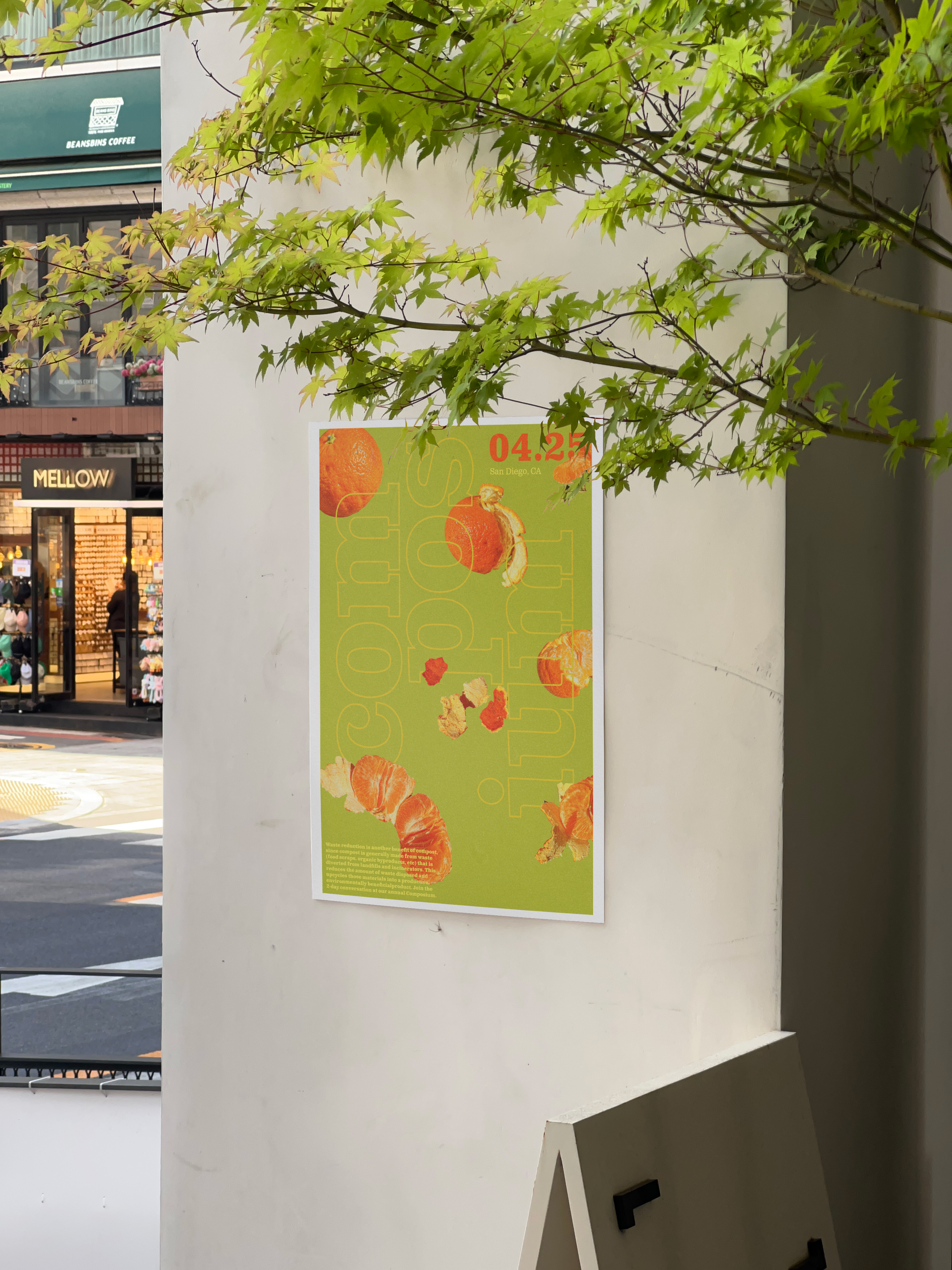 Poster of oranges on a green background on a gray wall with leaves from a tree in front